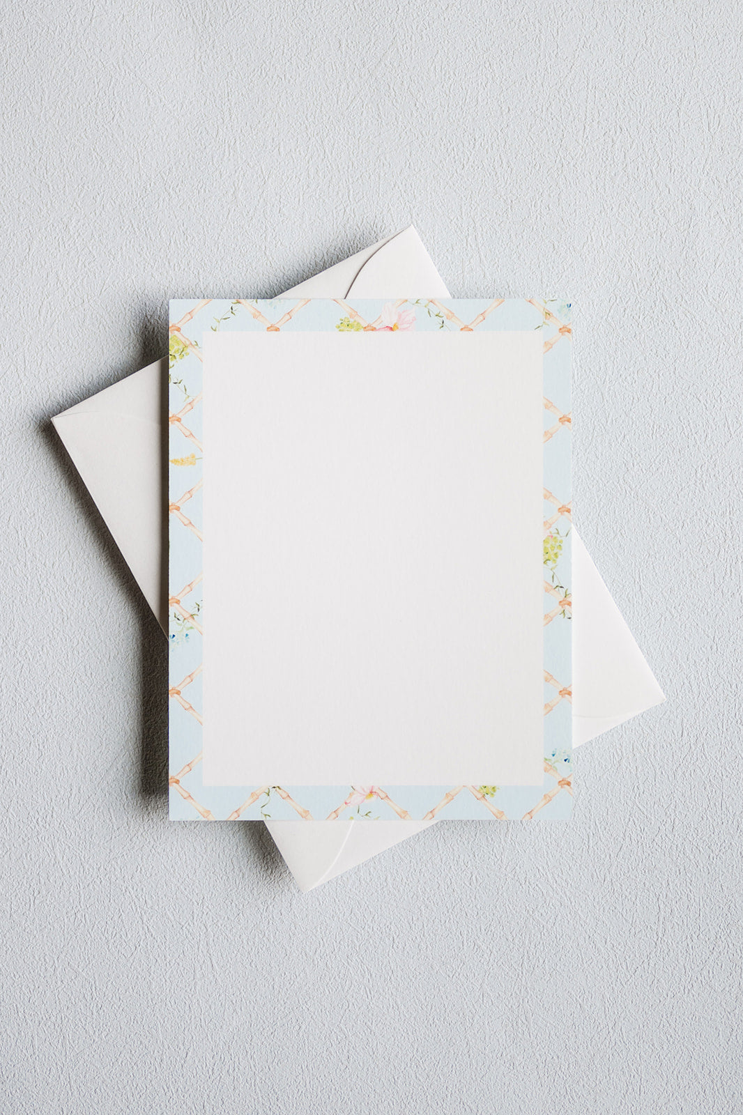 A stack of white stationery cards with a delicate pastel floral border, shown on a light gray textured background.