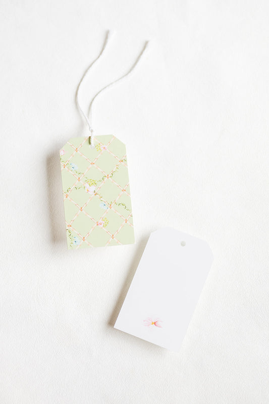 Two gift tags on a white textured background, with one tag featuring a pale green floral pattern and a white string, and the other being plain white.