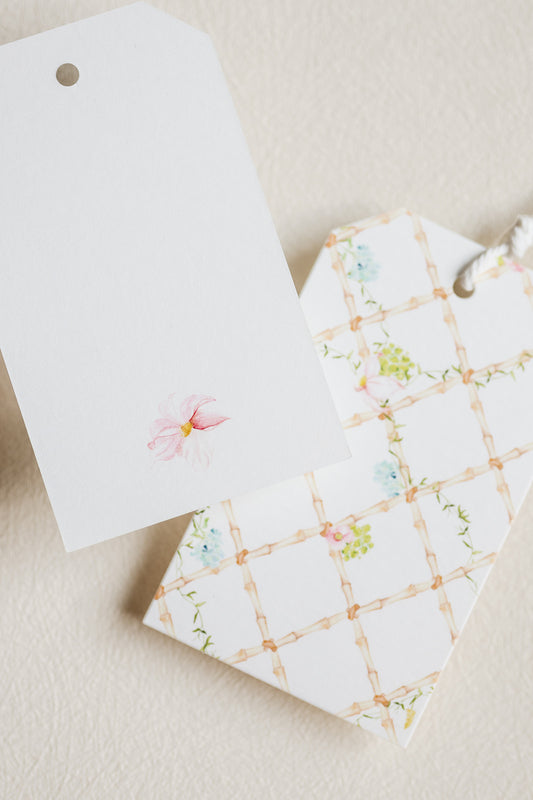 Two decorative gift tags on a textured cream background. One tag is plain white with a small pink flower illustration.