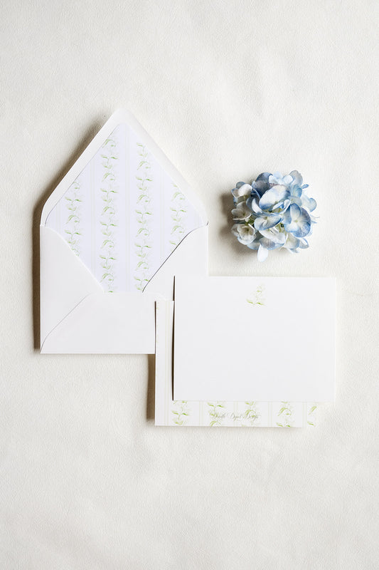 White stationery set with a matching envelope, card, and small floral embellishment on a light neutral background.