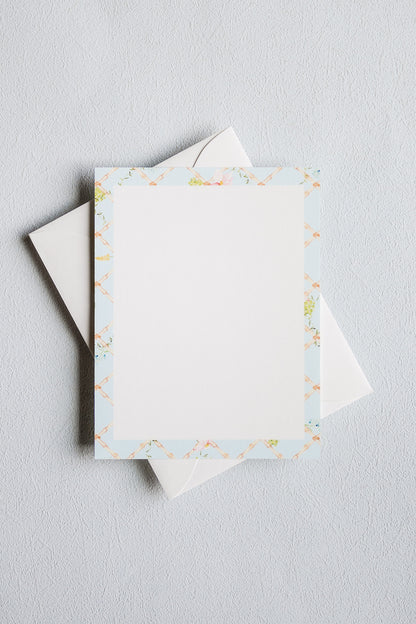 A stack of white stationery cards with a delicate pastel floral border, shown on a light gray textured background.