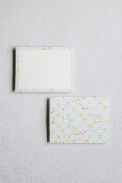 Two rectangular paper envelopes or cards with a pale blue border patterned with a subtle lattice and small floral motifs, shown on a light gray textured background.