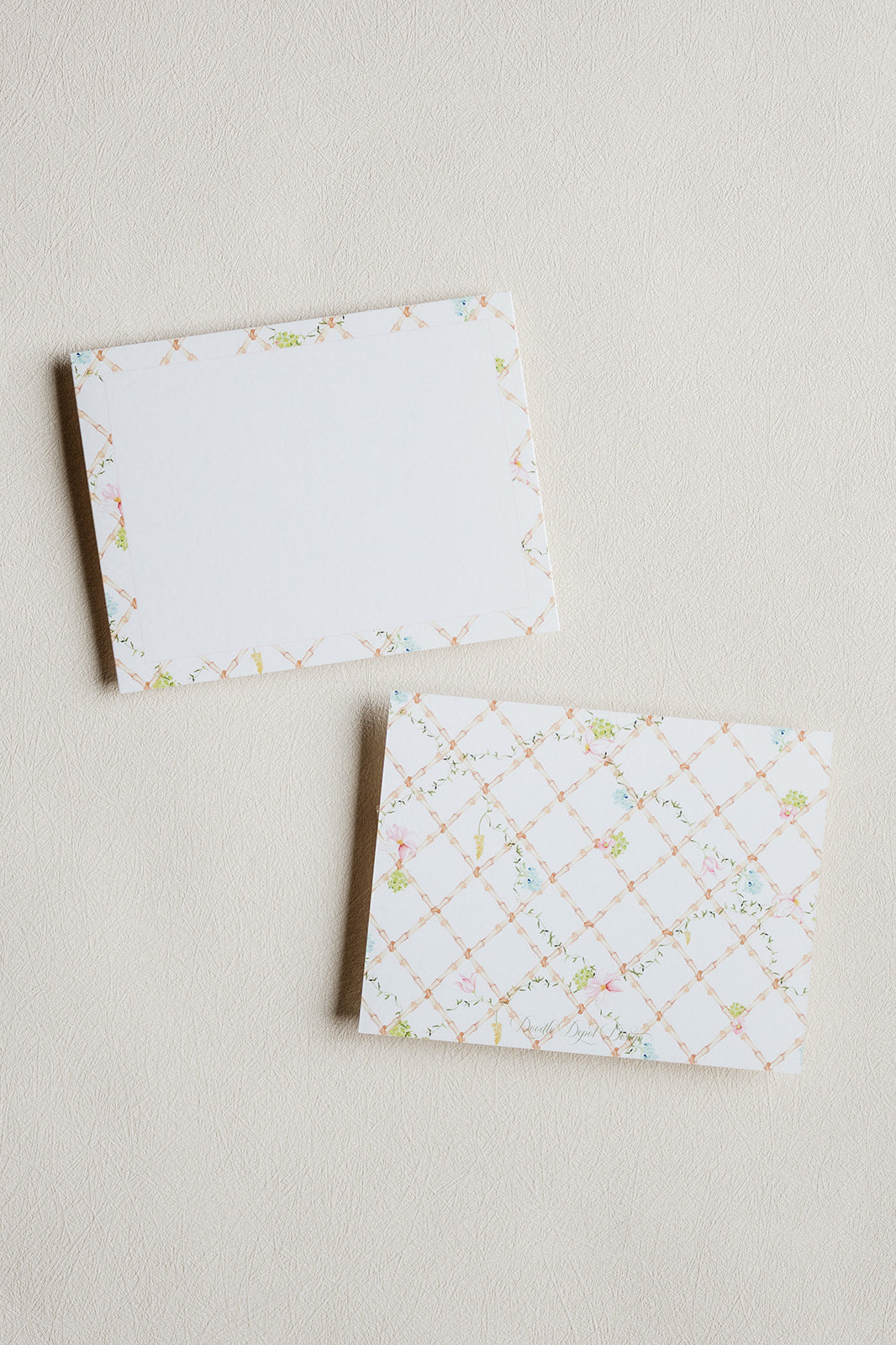 Two small rectangular cards or envelopes with delicate pastel floral and lattice border designs, arranged on a light beige textured background.