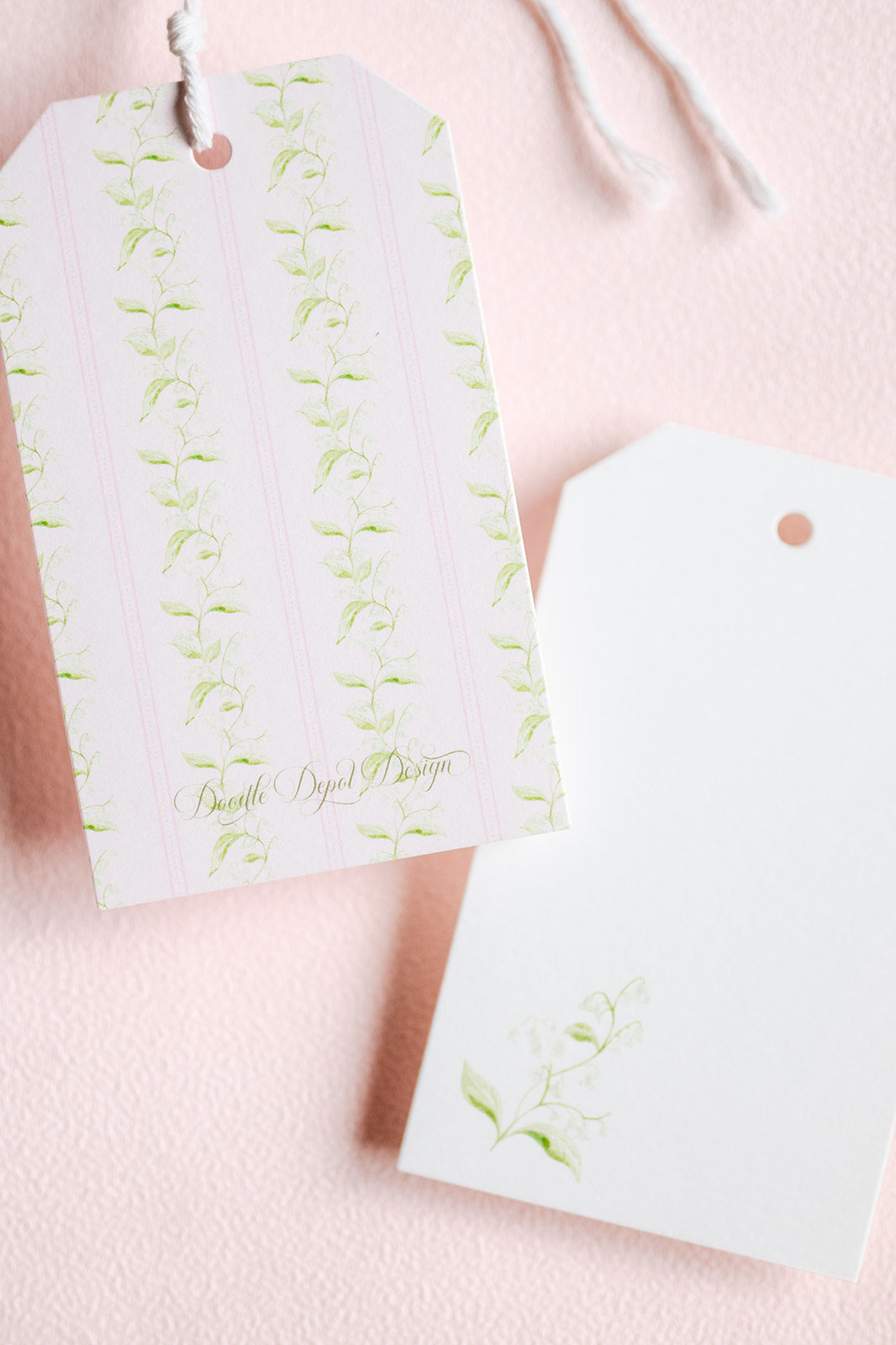 Two decorative gift tags on a soft pink textured background. One tag has pale pink vertical stripes with light green leafy vine illustrations and gold script text reading 'Breathe By: Jewel Designs.