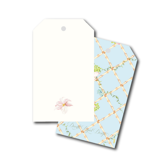 Two decorative gift tags on a plain white background. The front tag is off-white with a small pale pink flower illustration near the bottom and a hanging hole at the top.