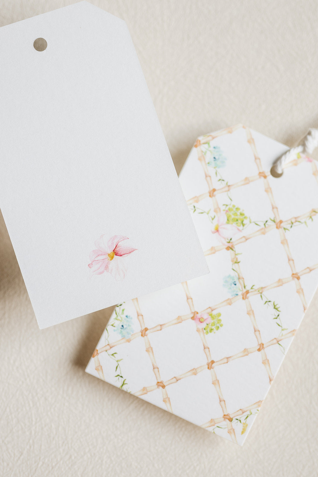 Two decorative gift tags on a textured cream background. One tag is plain white with a small pink flower illustration.