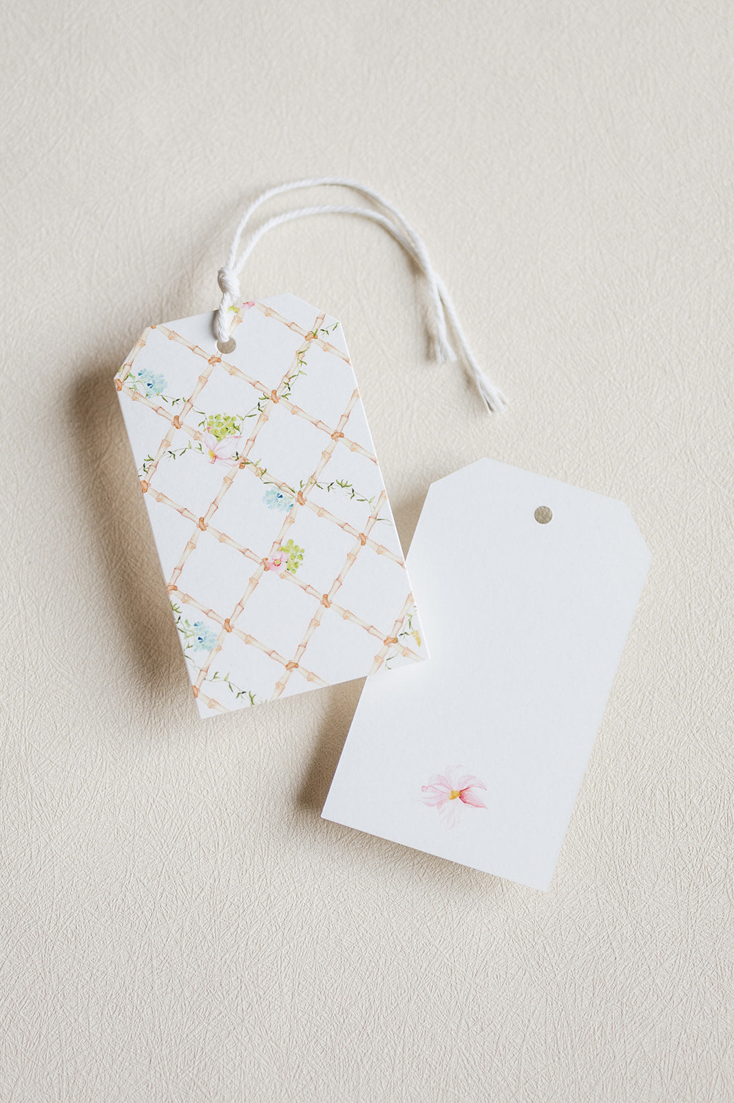 Two decorative gift tags on a textured beige background. One tag has a white base with a light peach lattice pattern and small pastel floral accents.