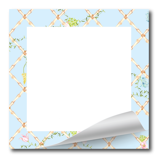 A square notepad or memo pad with a light blue border decorated with a gold trellis pattern and small floral accents, featuring a large blank white writing area and a curled bottom-right corner.