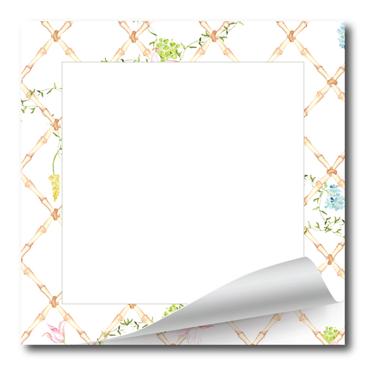 A square white notepad or memo pad with a decorative border featuring a light tan lattice pattern and small watercolor flowers in green, blue, pink, and yellow. The bottom-right corner is curled up to show a white page underneath, set against a clean white background.