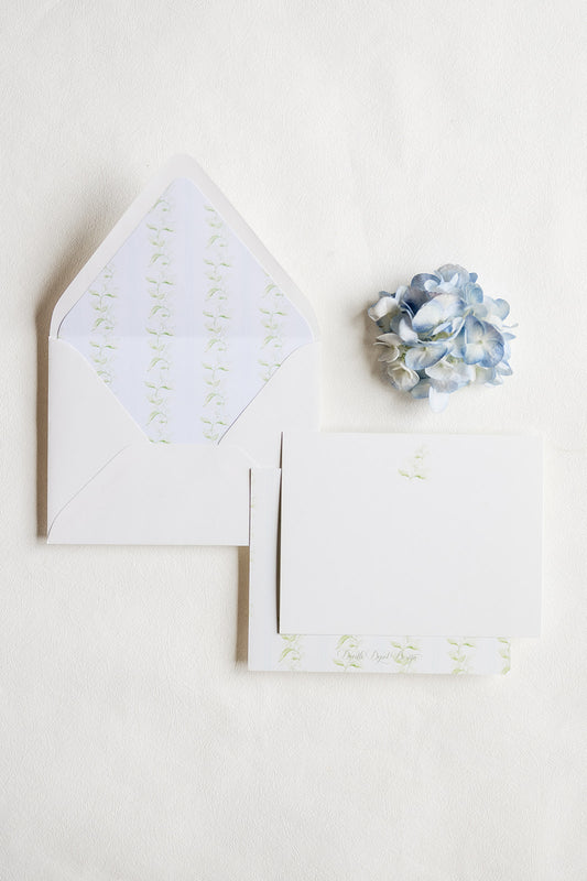 White stationery set with a matching envelope, card, and small floral accent on a light neutral background.