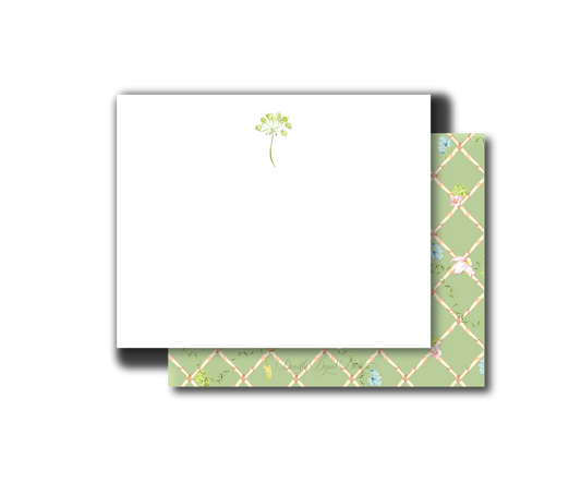A white stationery card with a small green floral illustration near the top, shown with a matching patterned envelope behind it on a light gray background.