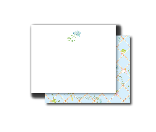 A white stationery card with a small blue and green floral illustration near the top left, layered over a light blue patterned envelope or backing with a gold trellis design and cursive script.